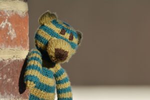 Photograph of a worn out green and yellow stripped teddy bear looking sad